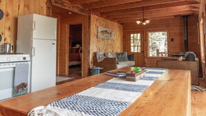 L’intérieur d’une cabane en bois comprend une longue table à manger, un réfrigérateur, une cuisinière et un ventilateur de plafond.
