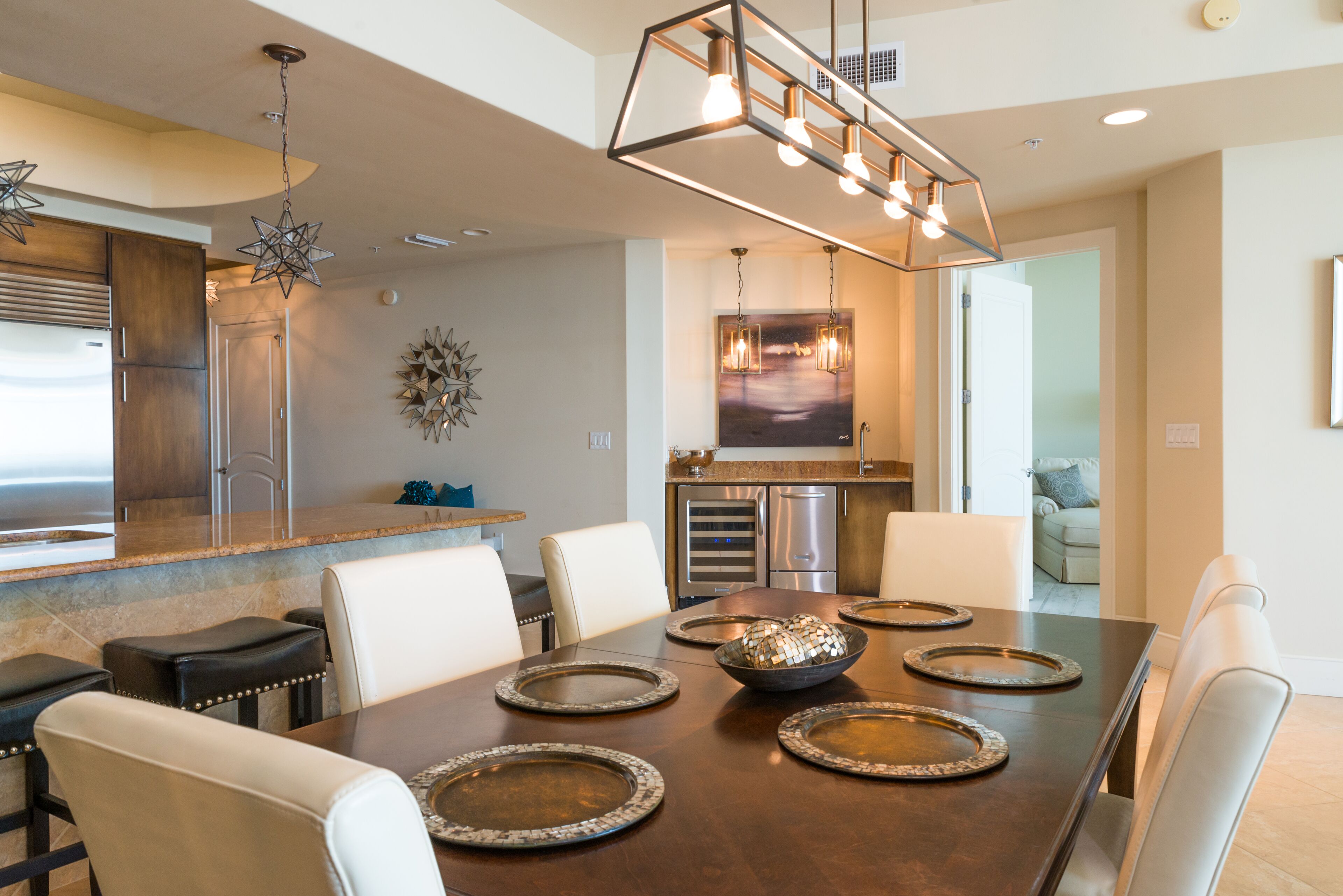 A modern dining area with a large wooden table, white chairs, and a contemporary chandelier.