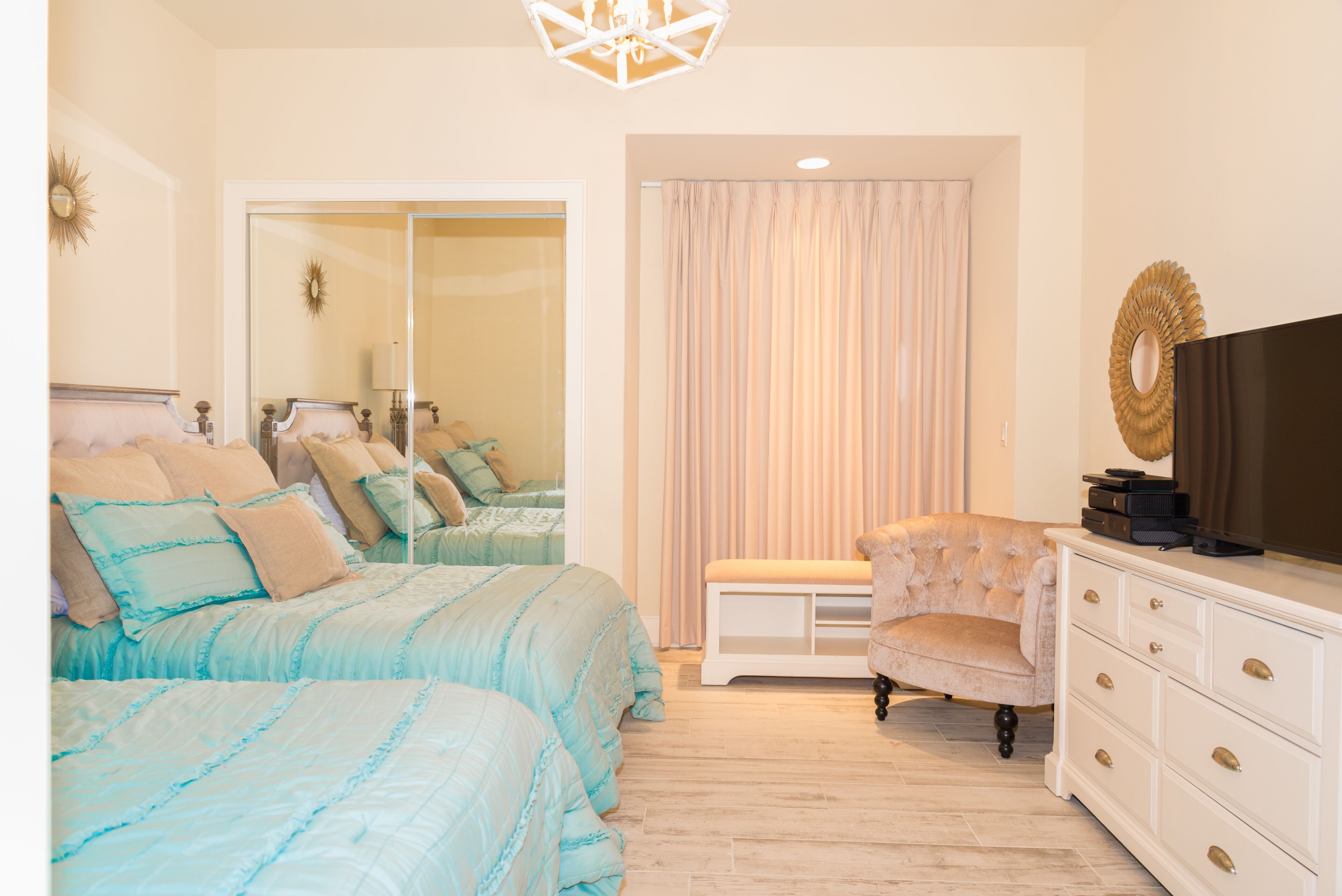 A bedroom with two beds, a vanity with a mirror, a bench, and a television.