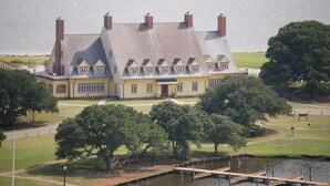 A large, multi-story building with a symmetrical facade, a central entrance, and a dock extending into a body of water. - Beautiful Oceanside Property W/Pool in Great Beach Location! (Corolla)