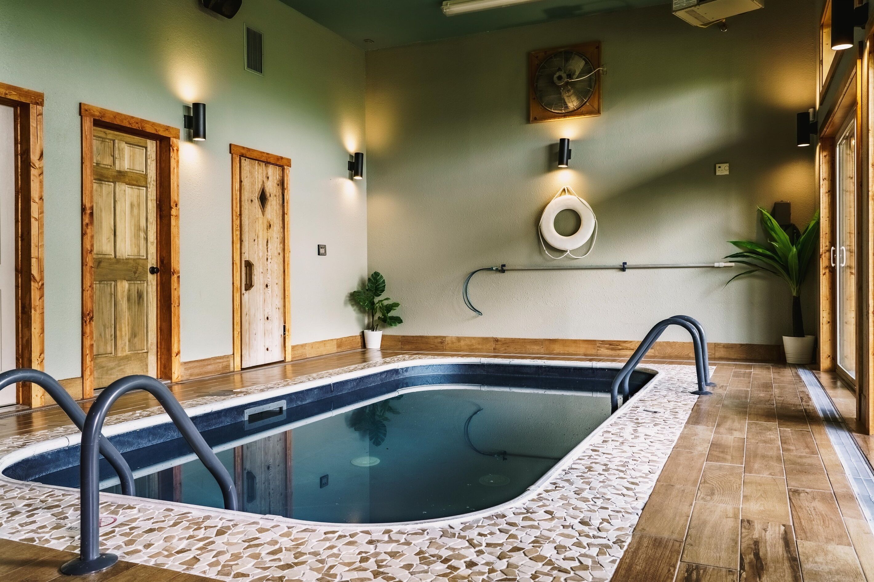 A swimming pool with a tiled deck, wooden doors, and wall-mounted lighting fixtures.