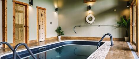 A swimming pool with a tiled deck, wooden doors, and wall-mounted lighting fixtures.