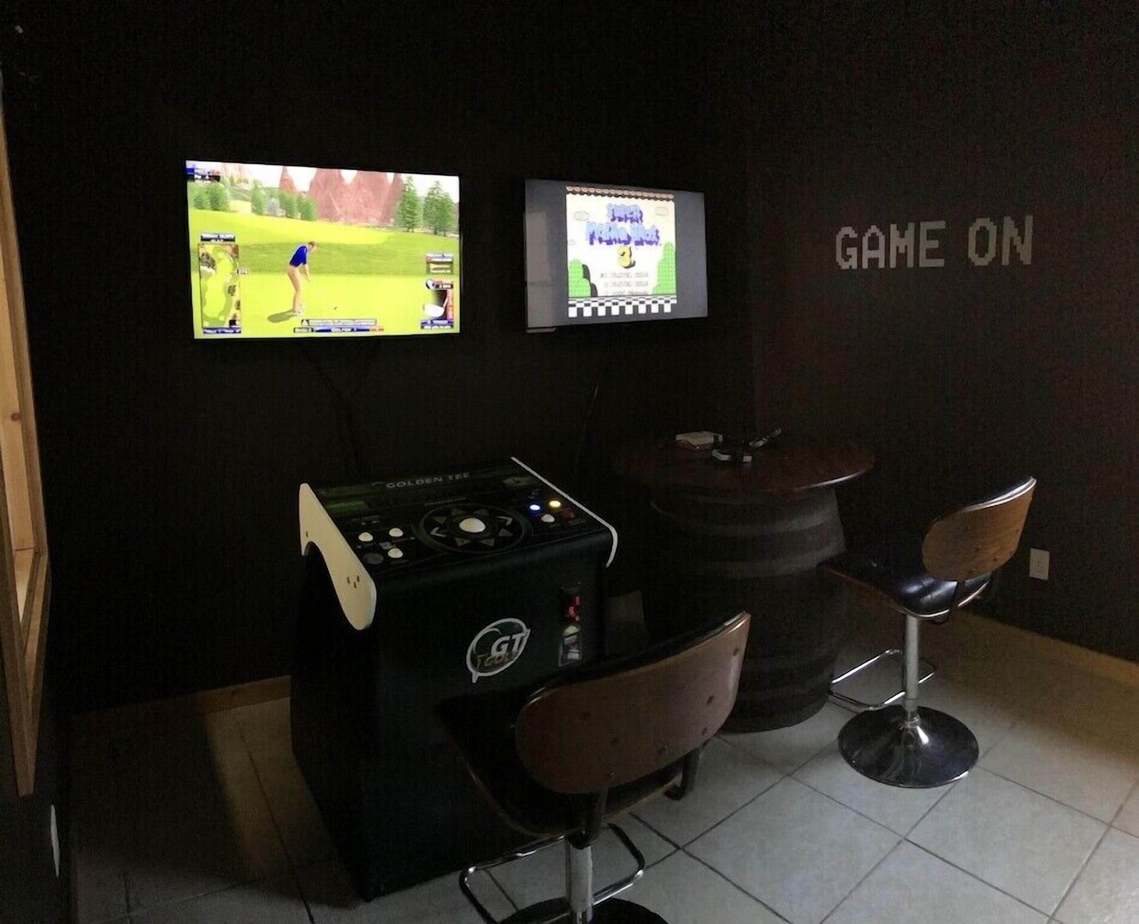 Un espace de jeu équipé de deux écrans, d’une console de jeux et de deux tabourets de bar.