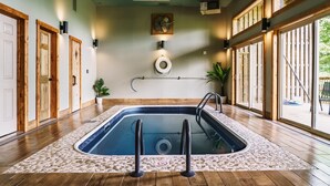 Piscina con suelo de madera, rodeada de amplios ventanales, y equipada con una escalera y un flotador de seguridad.