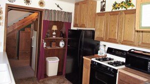 A compact kitchen with wooden cabinets, a black refrigerator, a stove, and a trash bin. - Sky View Log Cabin- Off the beaten trail yet close to all the main attractions! (Custer)