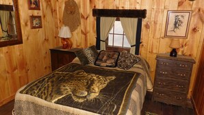 A wooden-paneled room with a bed featuring a leopard print bedspread, a wooden dresser, and a window with curtains. - Sky View Log Cabin- Off the beaten trail yet close to all the main attractions! (Custer)