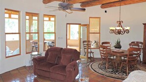 A spacious living room with a brown sofa, a dining table with chairs, a chandelier, and large windows allowing natural light. - On the Pecos River in Pecos New Mexico (Pecos)