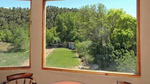 A room with large windows offering a view of a green lawn and trees. - On the Pecos River in Pecos New Mexico (Pecos)