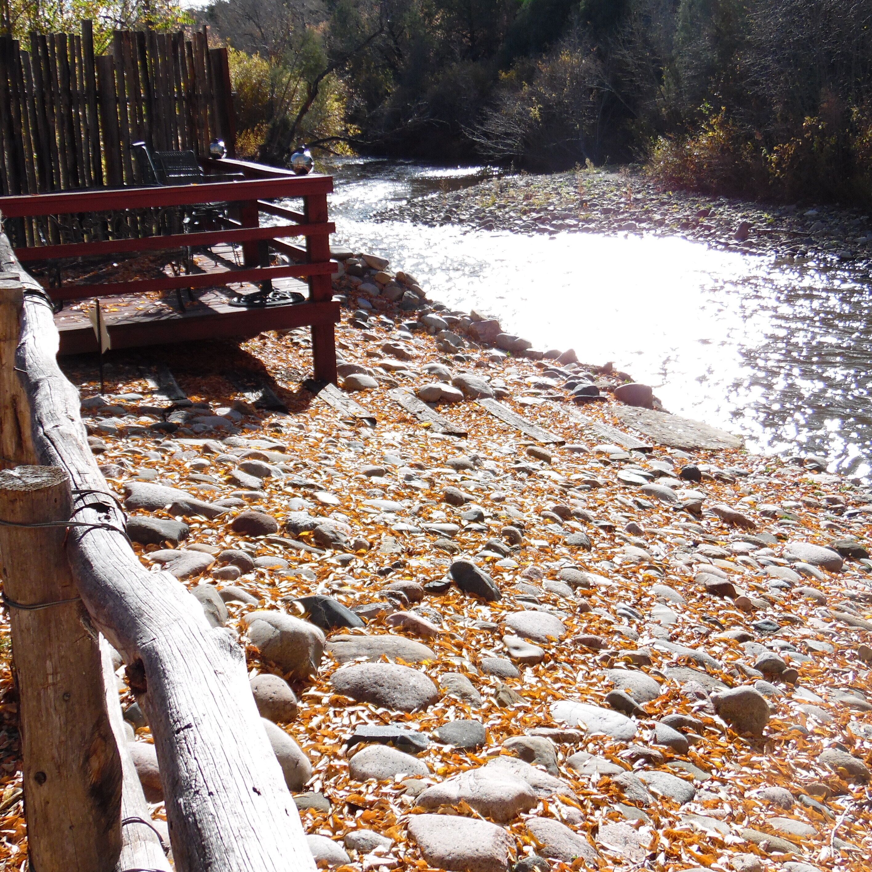 A wooden bench by a river with a rocky shore.