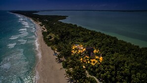 Eine Luftaufnahme eines Strandes mit einer kleinen Hotelanlage, einigen Gebäuden und Palmen.