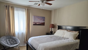 A bedroom with a bed, a chair, a ceiling fan, a nightstand with a lamp, and a painting on the wall. - Near Cardinals Stadium, Texas Rangers Stadium, Golf, NASCAR and Hiking    (Surprise)
