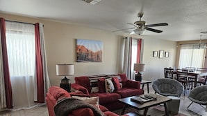 A living room with a red sofa, two lamps, a coffee table, a ceiling fan, and a dining area with chairs and a table. - Near Cardinals Stadium, Texas Rangers Stadium, Golf, NASCAR and Hiking    (Surprise)
