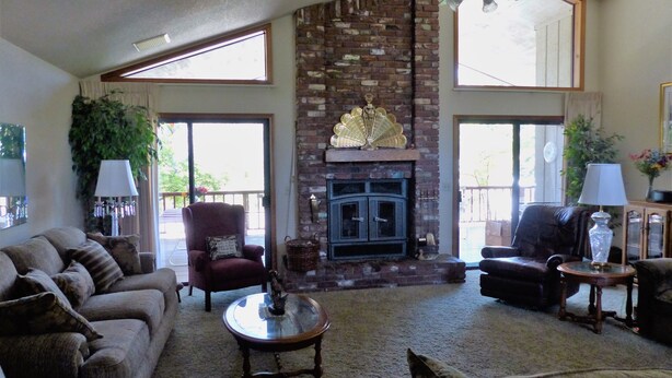 A living room with a fireplace, a ceiling fan, and a large window. - SIERRA ESCAPE! SPACIOUS COUNTRY HOUSE WITH POOL & SPA--20 MINUTES FROM YOSEMITE! (Oakhurst)