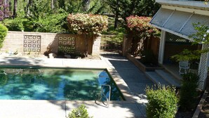A swimming pool surrounded by a wooden fence, a brick wall, and lush greenery. - SIERRA ESCAPE! SPACIOUS COUNTRY HOUSE WITH POOL & SPA--20 MINUTES FROM YOSEMITE! (Oakhurst)