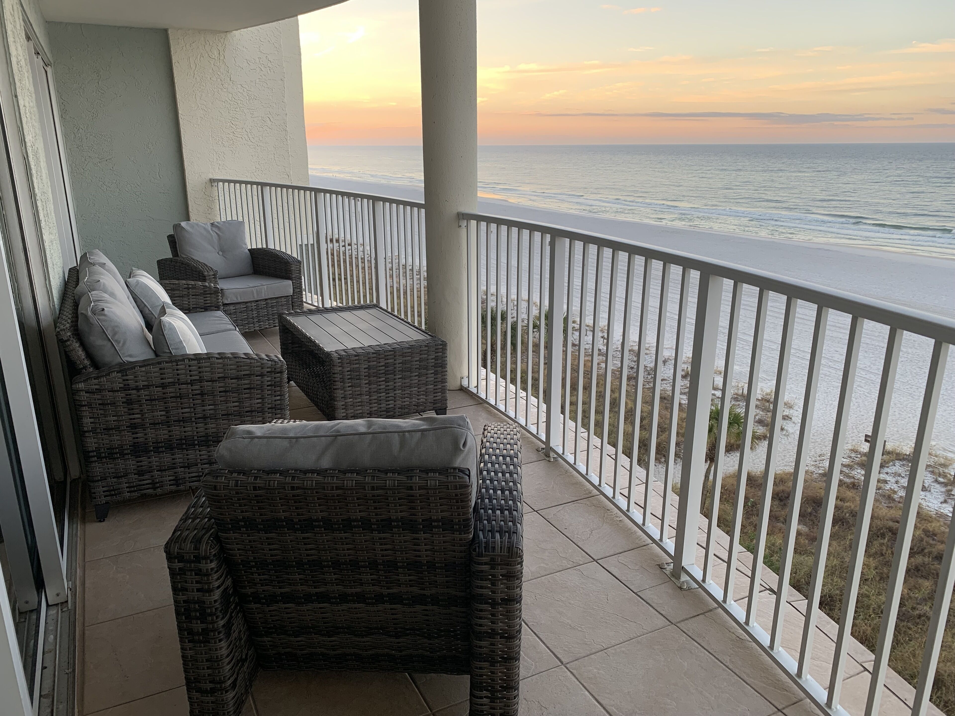A balcony with wicker furniture and a view of the ocean at sunset.