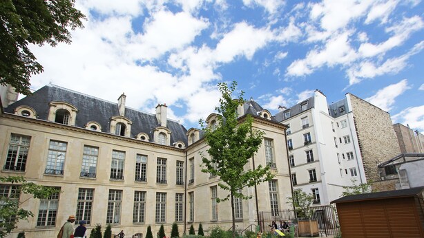 Un edificio histórico con arquitectura clásica, que presenta un patio central con un árbol y un sendero.