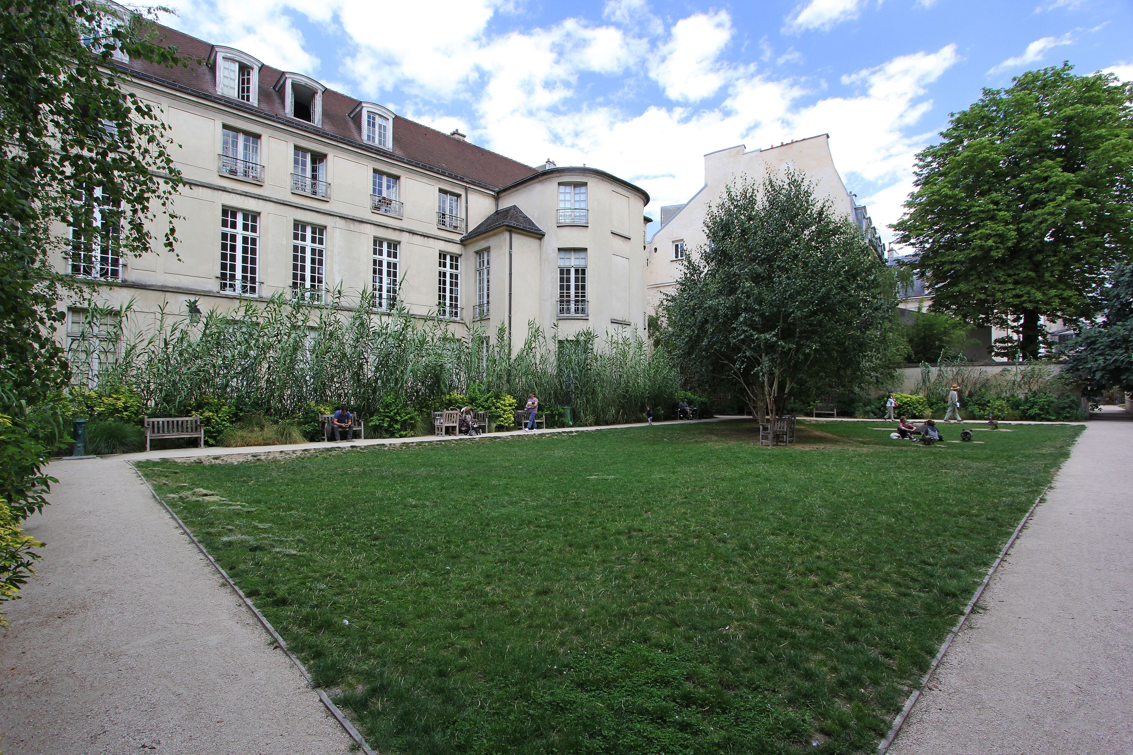 A courtyard with a lawn, a pathway, and a building with multiple windows and balconies.
