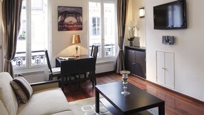 Una sala de estar con un sofá, una mesa, un televisor y un cuadro de la Torre Eiffel.
