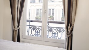 Una habitación con ventana, cortinas y vistas a un balcón con barandilla.