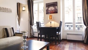 Habitación de hotel con sofá, una mesa de comedor con sillas, un jarrón de cristal decorativo y un cuadro con la Torre Eiffel.