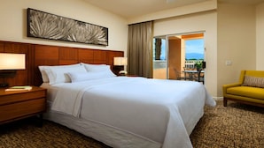A hotel room with a large bed, a nightstand, a desk, a chair, and a view of the outdoors.