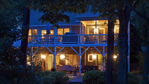A two-story house with a balcony, a staircase leading to the entrance, and a well-lit porch area. - Lakefront Luxe Retreat in Tranquil Cove  Endless Enjoyment  Lakeside Fireplace (New London)