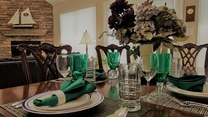 A dining table set with green napkins, plates, and glasses, a vase of flowers, and a ship model on a brick wall. - Lakefront Luxe Retreat in Tranquil Cove  Endless Enjoyment  Lakeside Fireplace (New London)