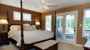 A bedroom with a four-poster bed, two bedside tables with lamps, a bench, and a sliding glass door leading to a balcony. - Lakefront Luxe Retreat in Tranquil Cove  Endless Enjoyment  Lakeside Fireplace (New London)