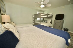 A bedroom with bunk beds, a television, a desk, and a ceiling fan.