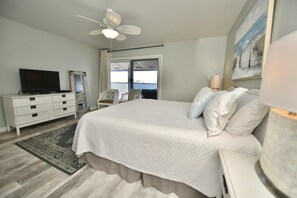 A bedroom with a bed, a television, a ceiling fan, a dresser, and a window with a view. - A 24 Sundown Condominiums (Pensacola)