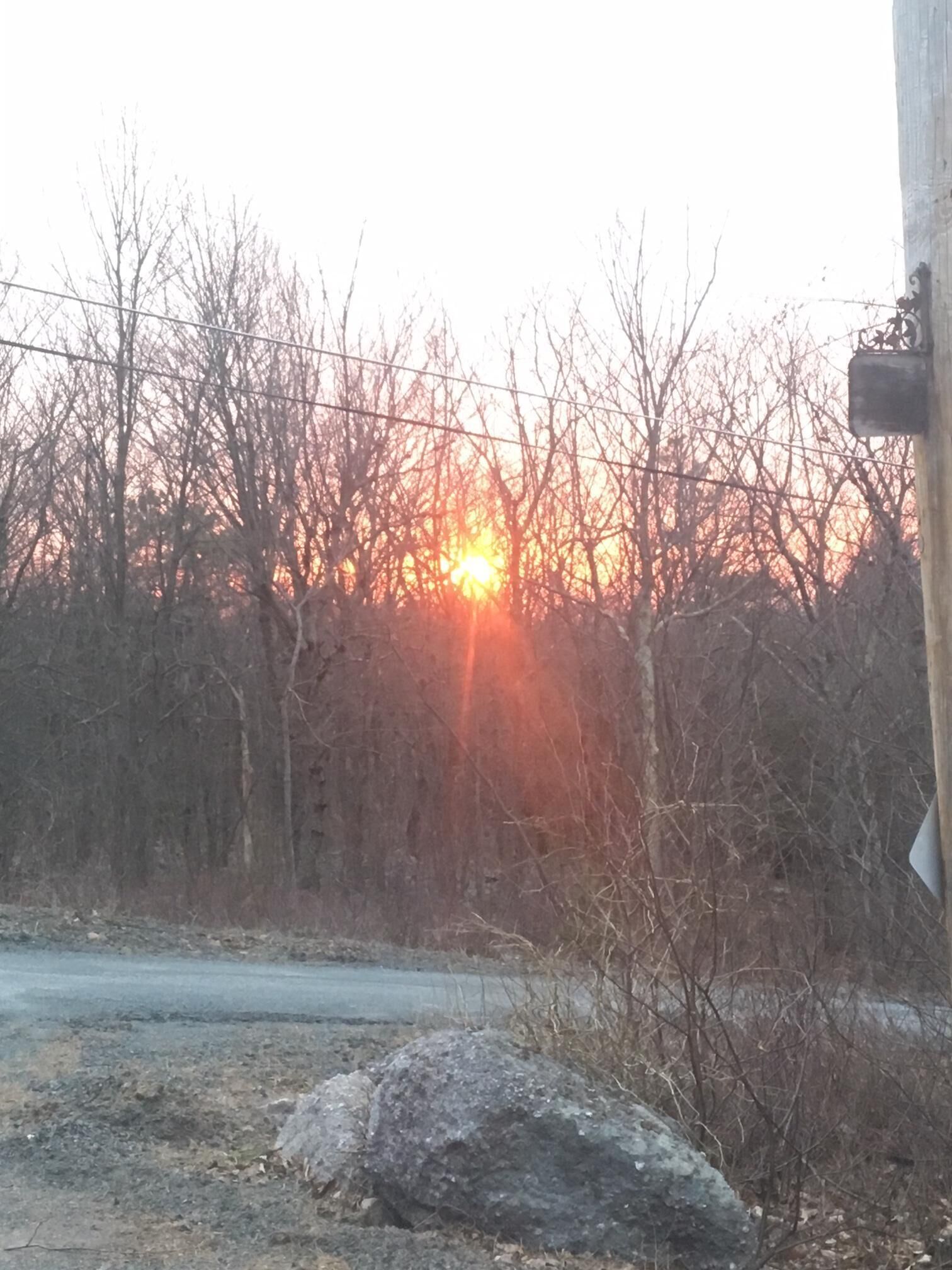 Un atardecer sobre un paisaje árido con una carretera y una gran roca al frente.