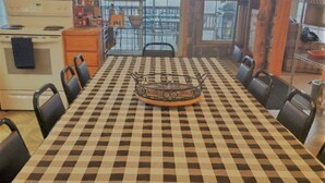 A dining area with a checkered tablecloth, chairs, a central decorative item, and a view of the outside through large windows. - 4 Bedroom House - Great Views - Secluded Location (Jim Thorpe)