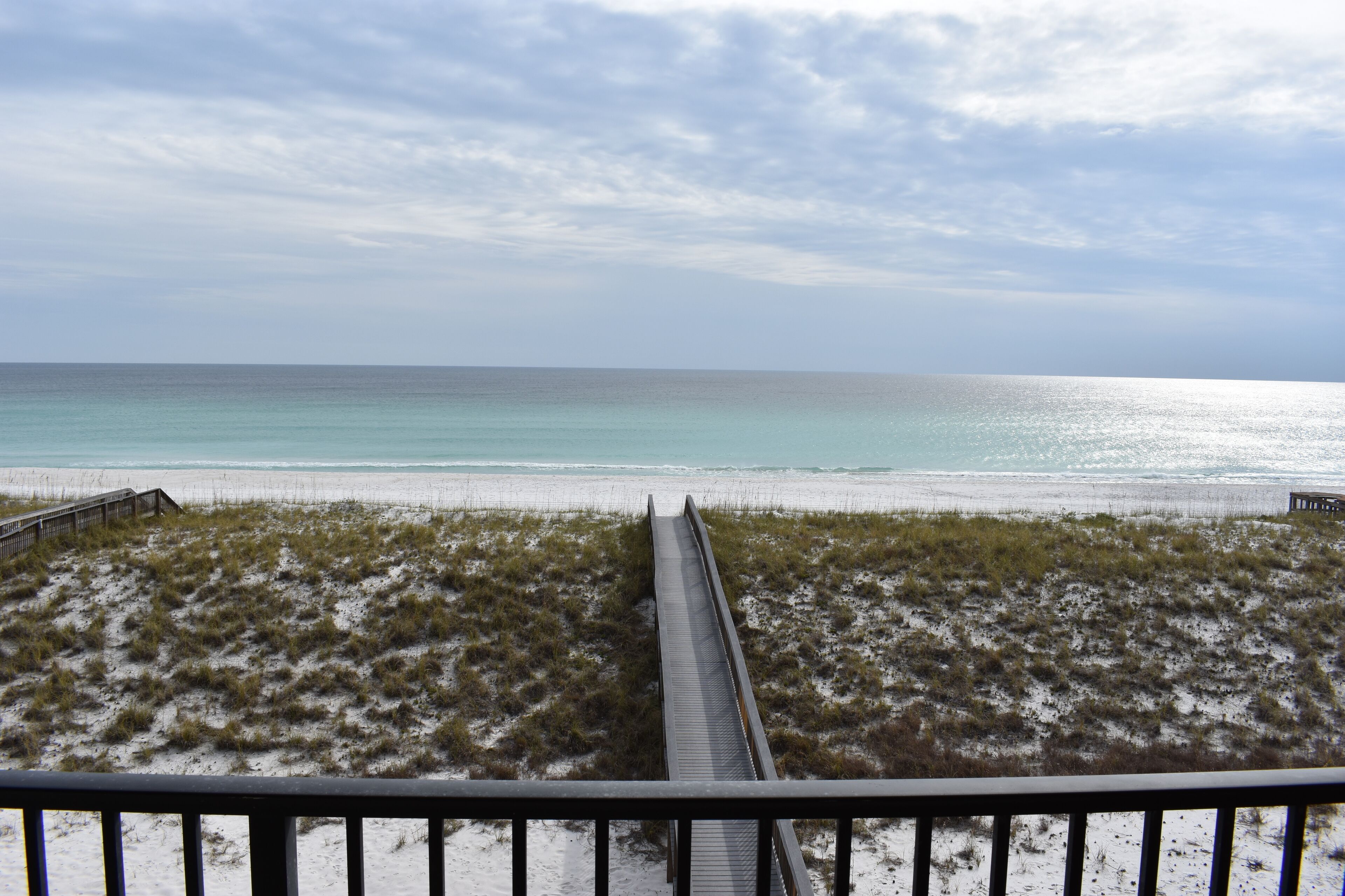 A beach with a wooden boardwalk leading to the shore, sandy dunes, and a clear view of the ocean.