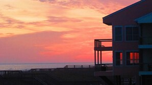 Un edificio con balcón que da a una playa al atardecer.