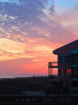 A building with a balcony overlooking a beach at sunset.