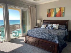 A bedroom with a large bed, a nightstand, a lamp, and a view of the ocean through a sliding door. - Oceanfront 4 bedroom 3 bath home for up to 10 guests -Your dream vacation awaits (Navarre)