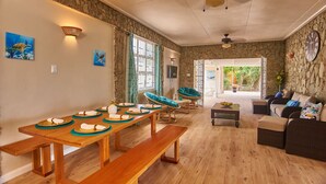 A spacious room with a wooden dining table set for four, a sofa, and a chair with a view to the outdoors.