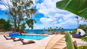 A pool area with lounge chairs, a small pool, and a view of the ocean.