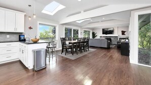 A spacious kitchen with white cabinets, a dining area with a table and chairs, and a living area with a sofa and TV.