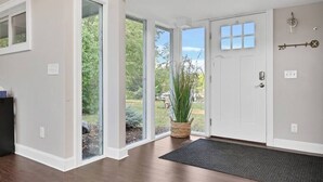 A spacious entryway with a large glass door leading to a garden, a potted plant, and a door with a key hanging on the wall.