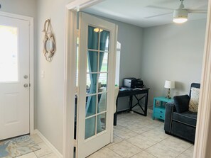 A room with a desk, a chair, a sofa, a door, and a ceiling fan.