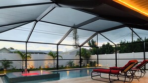 Une piscine extérieure dotée d’une structure en verre, de chaises longues et d’une petite table.