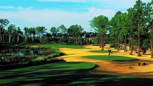 Un campo de golf con búnkeres de arena, un estanque y altos árboles.