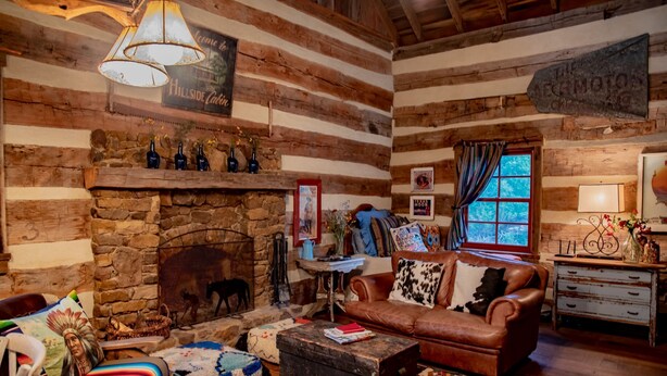 L’intérieur d’un chalet rustique, avec une cheminée en pierre, des murs en bois, un canapé en cuir et un coin salon confortable.