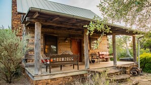 Une cabane rustique en rondins de bois, dotée d’un porche, d’un escalier en pierre et d’un espace salon extérieur.
