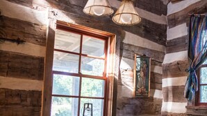 L’intérieur d’un chalet rustique en bois, avec une table à manger ronde, quatre chaises en bois, une grande fenêtre offrant une belle vue et un luminaire suspendu.