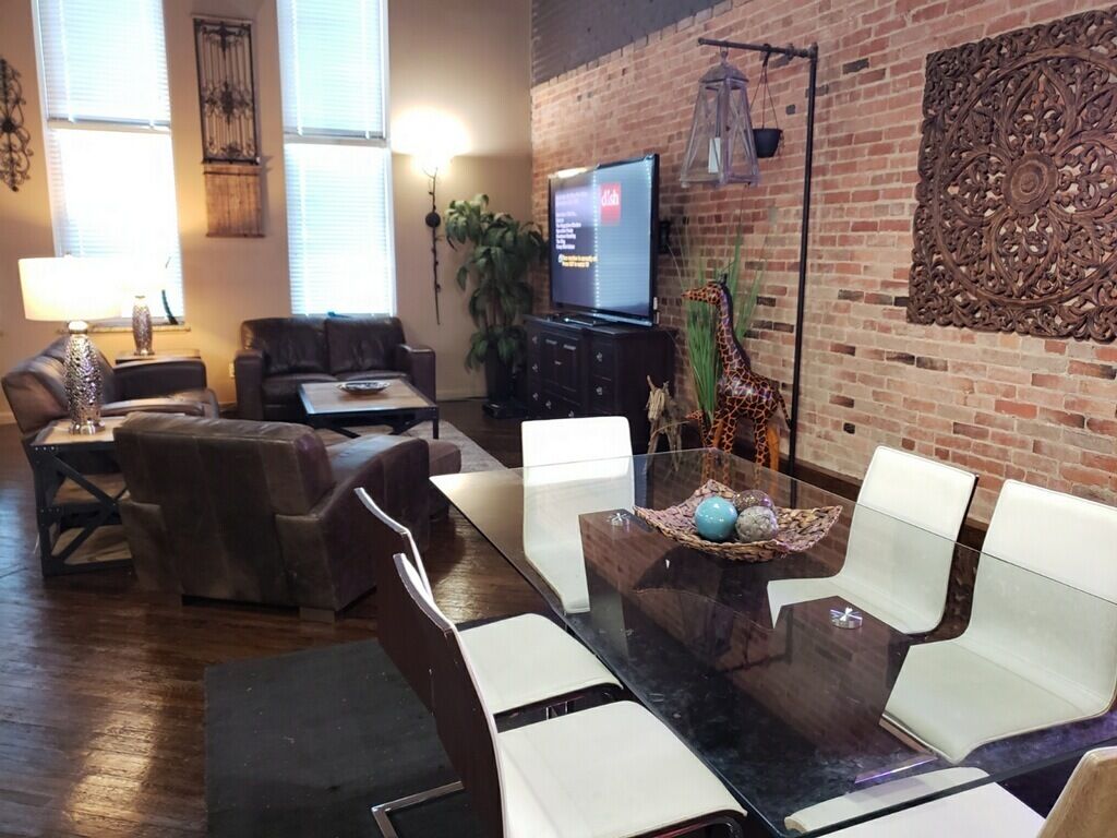 Un soggiorno moderno con un tavolo da pranzo in vetro, divani in pelle, una televisione e un muro in mattoni con decorazioni in metallo.