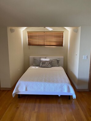Une chambre avec un lit, une fenêtre avec des stores et un coussin orné du mot « bonjour ».