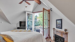 Ein Schlafzimmer mit Bett, Fernseher, Kamin und einem Balkon mit Blick auf Bäume.