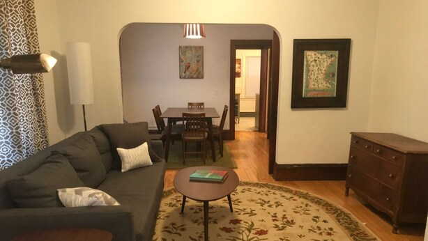 A living room with a sofa, a coffee table, a patterned rug, a dining table with chairs, and a dresser. - Cozy Seward Home - Close To Everything (Minneapolis)